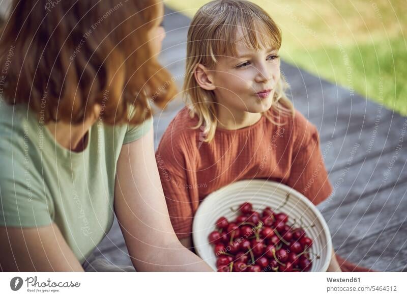 Close-up of mother and daughter eating cherries while sitting in yard color image colour image Germany leisure activity leisure activities free time