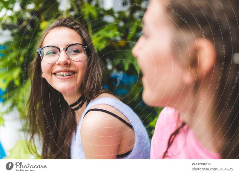 Happy teenage girl with braces and glasses looking at friend female friends eyeing dental brace Teenage Girls female teenagers woman females women happiness