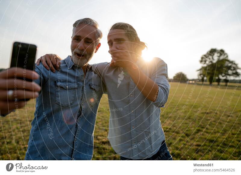 Excited father and adult son looking at smartphone on a meadow in the countryside human human being human beings humans person persons caucasian appearance