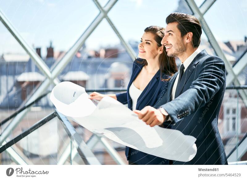 Smiling businesswoman and businessman holding plan in office offices office room office rooms plans smiling smile businesswomen business woman business women
