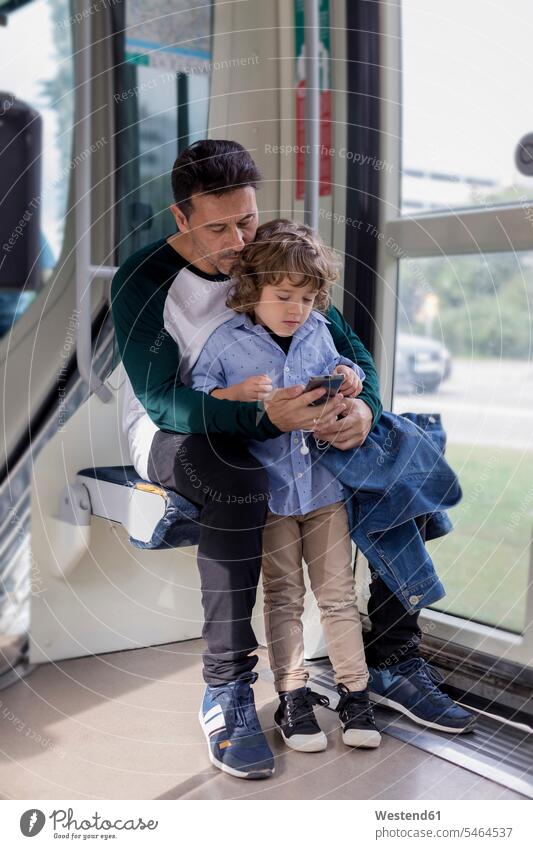 Father and son using cell phone in a tram father pa fathers daddy dads papa tramway tramways streetcars trams mobile phone mobiles mobile phones Cellphone