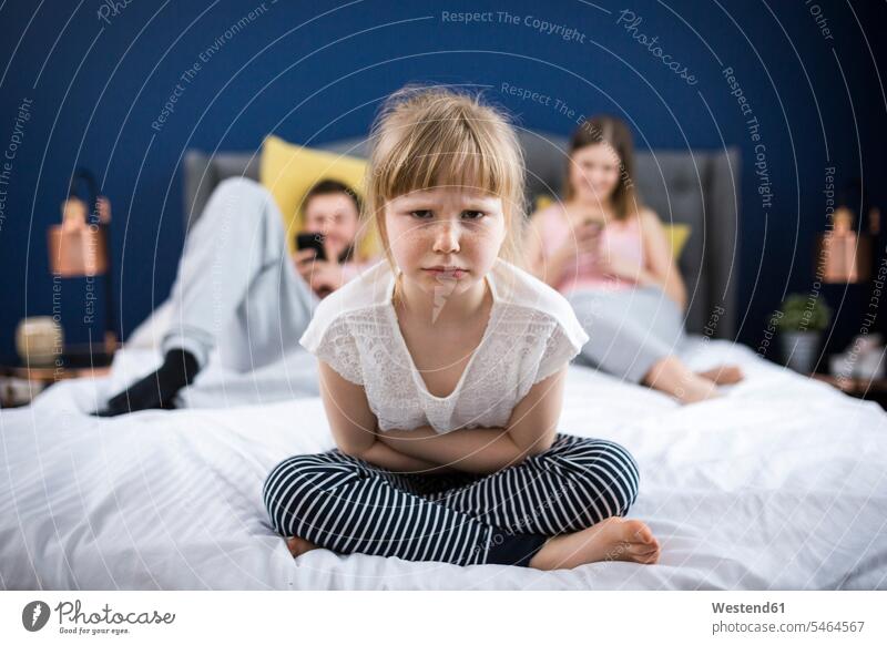 Angry little girl sitting on bed with her parents angry morose annoyed anger beds Boredom boring bored neglect Neglected neglecting family families Seated