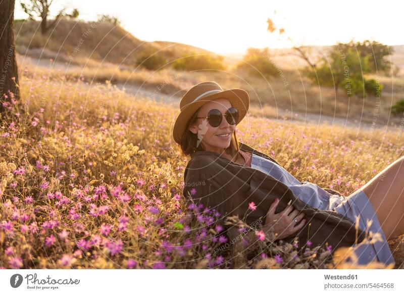 Young woman lying on meadow at sunset Eye Glasses Eyeglasses specs spectacles Pair Of Sunglasses sun glasses smile Seated sit in the evening relax relaxing