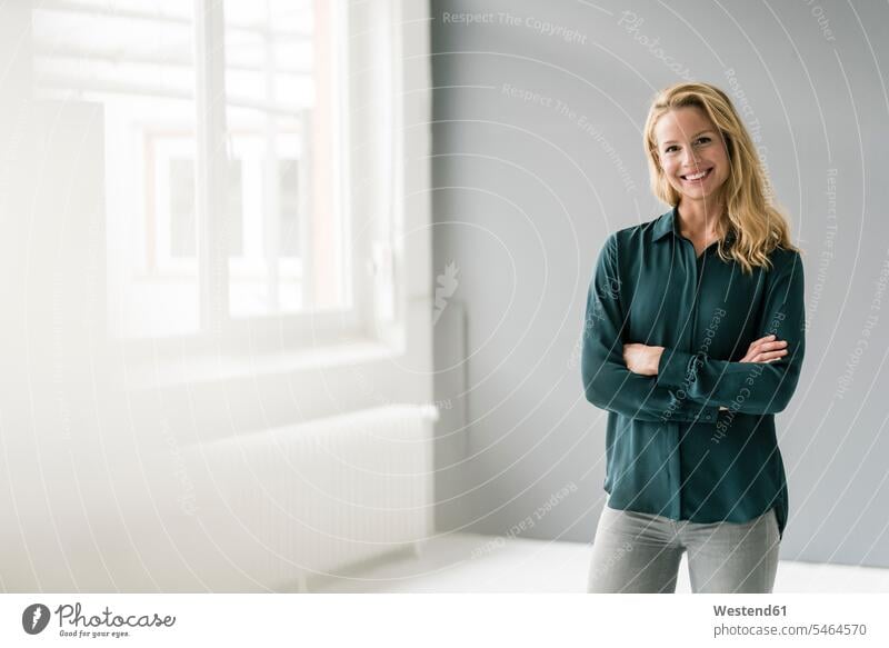 Successful, blond businesswoman standing in bright room, with arms crossed human human being human beings humans person persons caucasian appearance