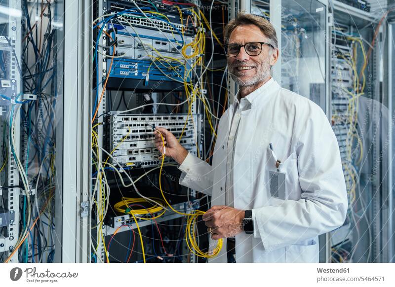 Smiling mature man plugging transceiver on fiber optic cable in data center color image colour image indoors indoor shot indoor shots interior interior view
