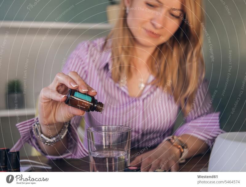 Close-up of businesswoman pouring essential oil in drinking glass at office color image colour image indoors indoor shot indoor shots interior interior view
