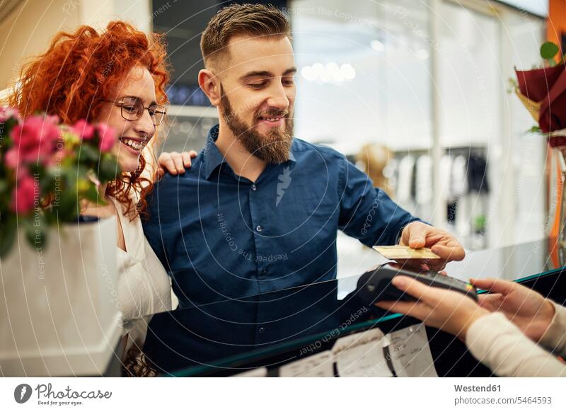 Happy couple paying at counter in flower shop customer clientele clients customers happiness happy twosomes partnership couples credit card debit card people