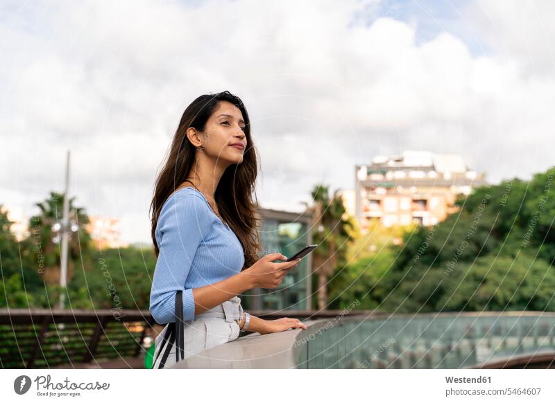 Thoughtful businesswoman holding mobile phone while standing on footbridge color image colour image Spain outdoors location shots outdoor shot outdoor shots day