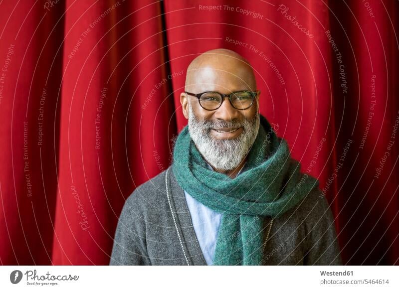 Portrait of smiling man wearing glasses and scarf in front of red curtain men males scarfs scarves portrait portraits smile specs Eye Glasses spectacles
