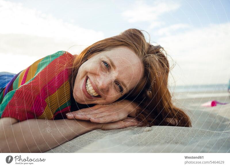 Redheaded woman lying in sand on the beach, with eyes closed beaches sandy smiling smile redheaded red hair red hairs red-haired females women laying down lie