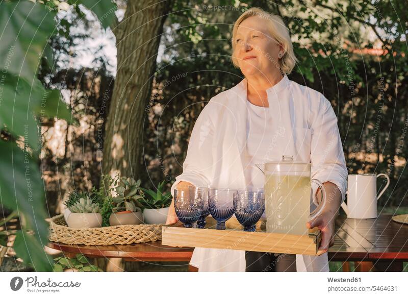 Thoughtful senior woman carrying tray with drinks while standing in yard color image colour image Spain leisure activity leisure activities free time