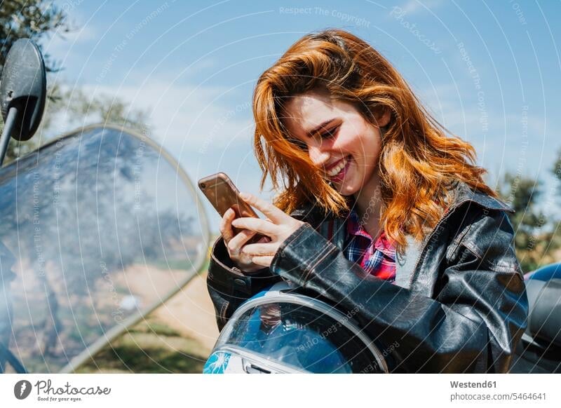 Portrait of happy redheaded woman on motorbike looking at cell phone, Andalusia, Spain motor vehicles road vehicle road vehicles Motor Cycle motorbikes