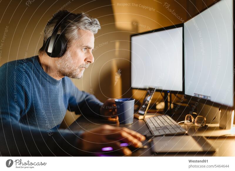 Mature man with headphones sitting at desk at home working on computer Occupation Work job jobs profession professional occupation jumper sweater Sweaters