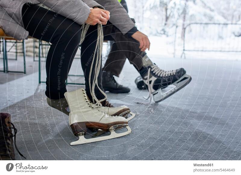 Couple sitting on bench at the ice rink, putting on ice skates couple twosomes partnership couples put on leg legs human leg human legs Seated ice skating