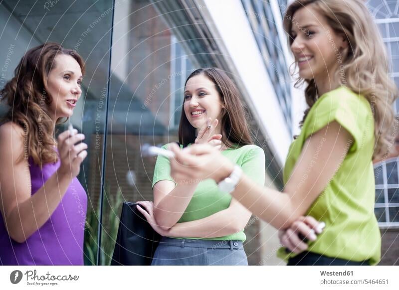 Female colleagues gossiping while smoking cigarettes during break outside office color image colour image outdoors location shots outdoor shot outdoor shots day