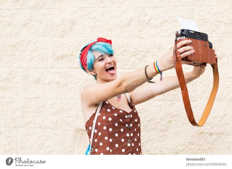 Portrait of young woman with blue dyed hair taking selfie with instant camera photograph photographs photos polaroid camera portrait portraits coloured females