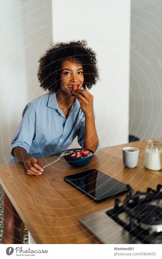 Woman using digital tablet and having a healthy breakfast in her kitchen morning in the morning sitting Seated smiling smile domestic kitchen kitchens use Fruit