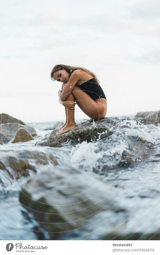 Beautiful young woman wearing swimsuit sitting on rock in the sea Swimming Costume bathing costume bathing costumes Swimming Suit bathing suit swimsuits