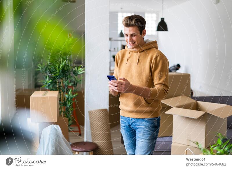 Smiling young man using mobile phone in messy living room during relocation color image colour image indoors indoor shot indoor shots interior interior view