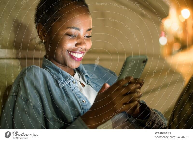 Portrait of happy young woman using smartphone in the city by night, Lisbon, Portugal human human being human beings humans person persons African black