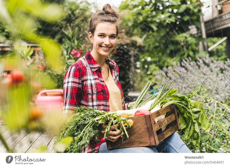 Smiling beautiful woman with vegetable crate sitting in community garden color image colour image Germany leisure activity leisure activities free time