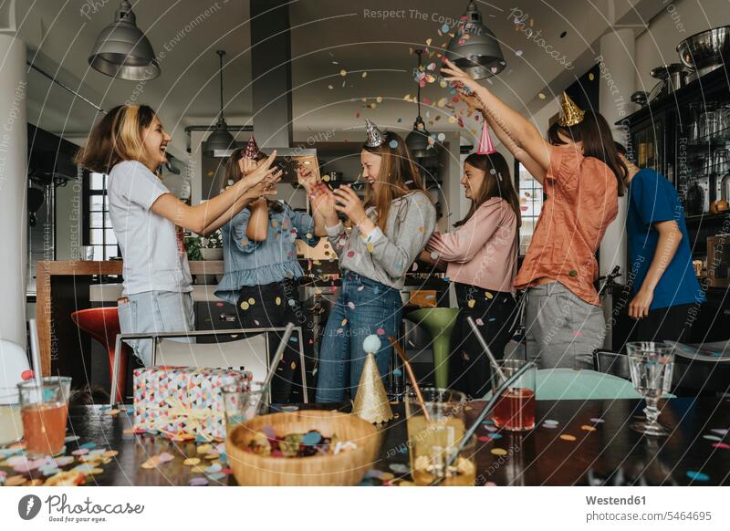 Cheerful friends throwing confetti on birthday girl while celebrating at home color image colour image Germany indoors indoor shot indoor shots interior