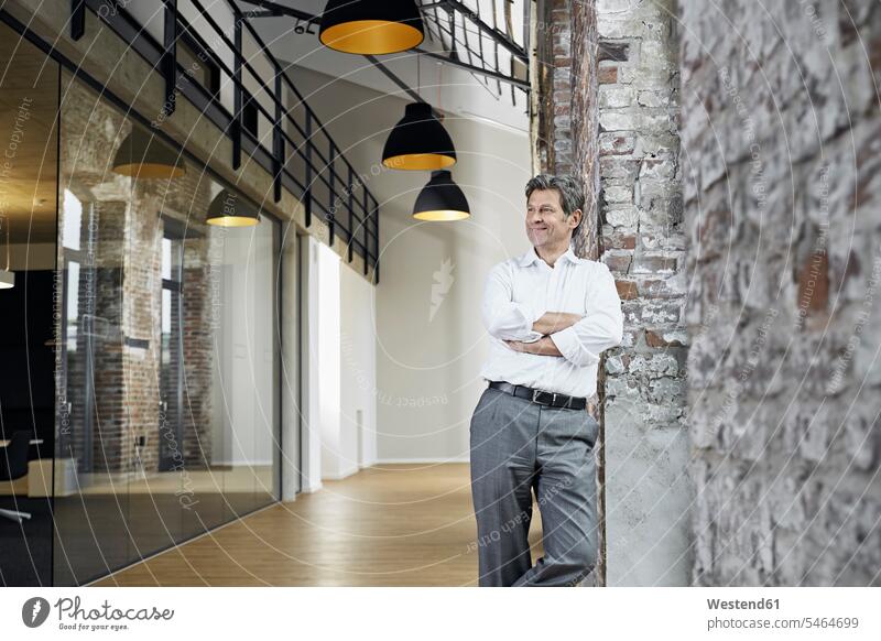Portrait of smiling businessman leaning against brick wall in modern office offices office room office rooms brick walls smile Businessman Business man