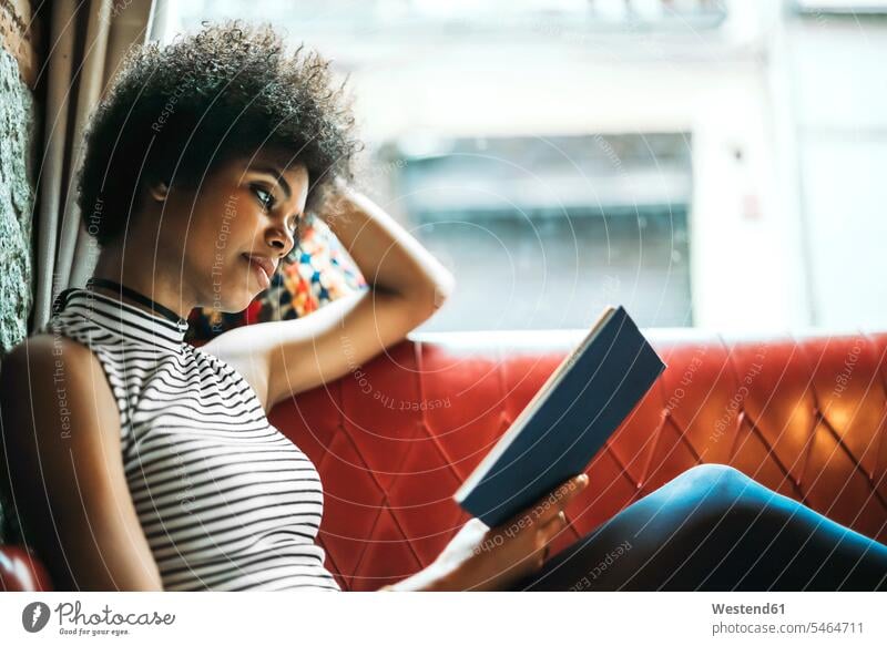 Mid adult woman with curly hair reading book while relaxing on sofa in cafe color image colour image indoors indoor shot indoor shots interior interior view