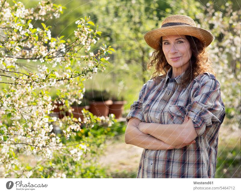 Portrait of smiling mature female farmer standing with arms crossed by tree at community garden color image colour image Germany outdoors location shots