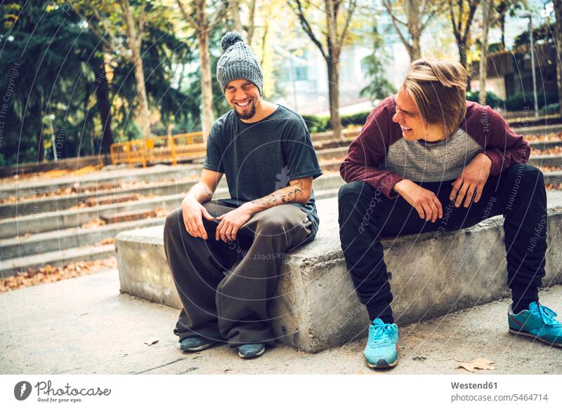 Cheerful male friends enjoying while sitting in park casual clothing casual wear leisure wear casual clothes Casual Attire color image colour image day