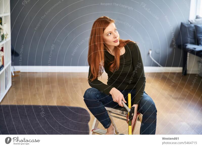 Redheaded woman with hammer and water level sitting on step ladder Seated spirit tool redheaded red hair red hairs red-haired females women hammers Step Ladder