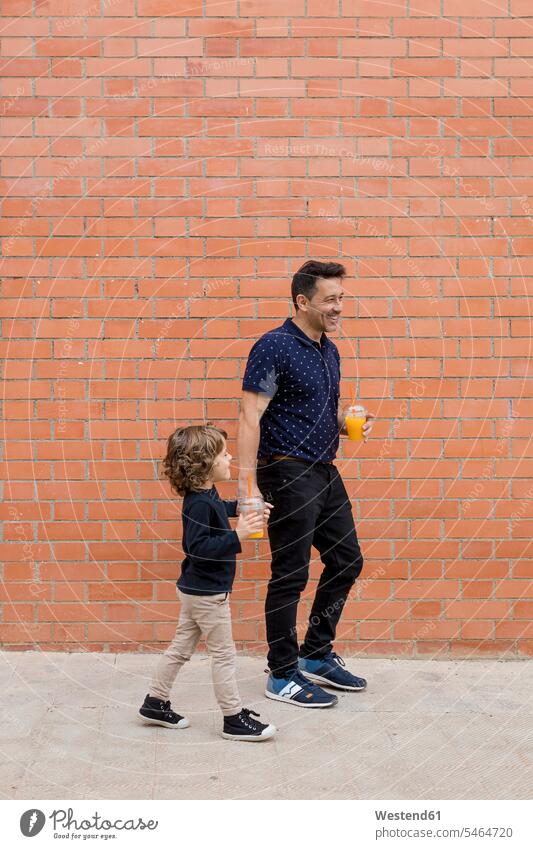 Father and son walking with soft drinks at brick wall refreshing drink refreshing drinks father pa fathers daddy dads papa going sons manchild manchildren