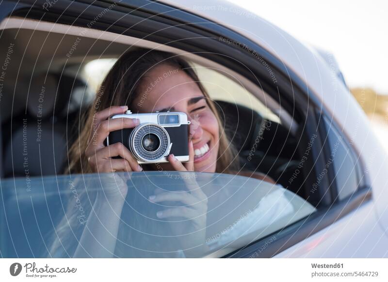 Woman sitting in car, taking pictures with a camera young women young woman excursion Getaway Trip Tours Trips cameras photographing automobile Auto cars