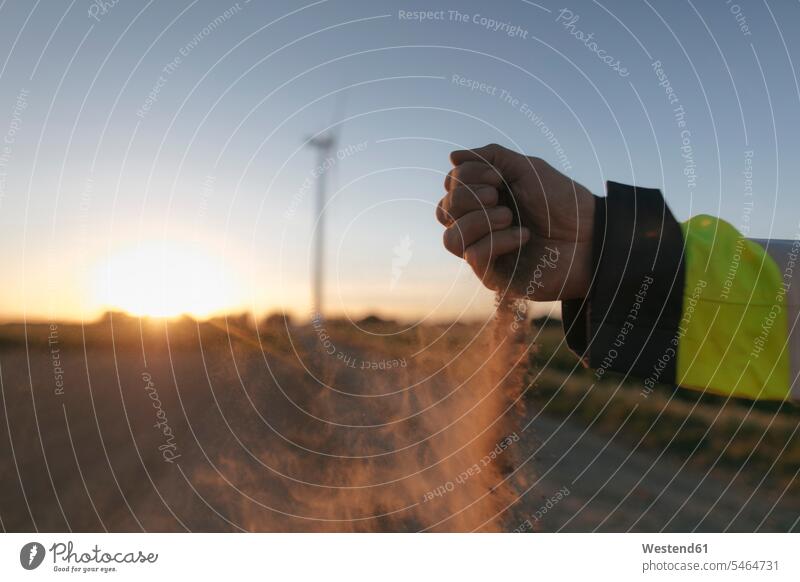 Close-up of man's hand scattering soil at a wind turbine at sunset wind turbines human hand hands human hands Field Fields farmland sunsets sundown engineer