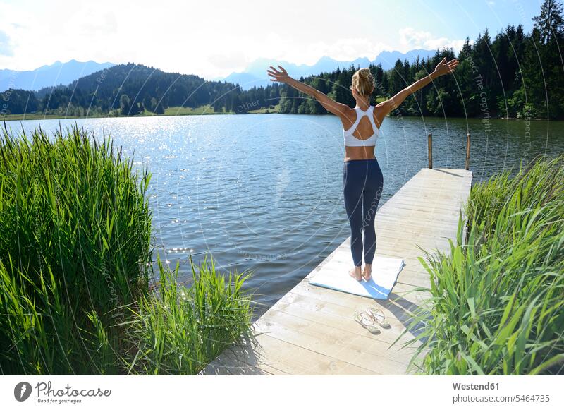 Germany, Mittenwald, back view of woman practising yoga on jetty at lake landing stage landing stages practicing practice practise exercise exercising lakes