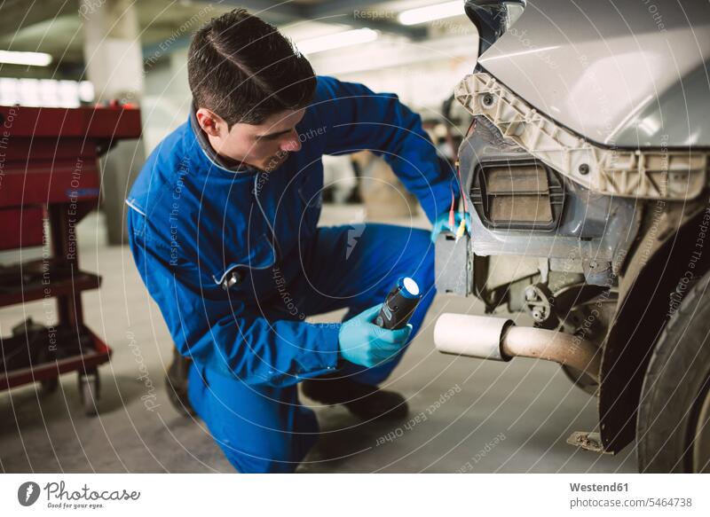 Mechanic inspecting a car with a torch in a workshop mechanic mechanician repairman mechanicians mechanists repairmen mechanics machinists automobile Auto cars