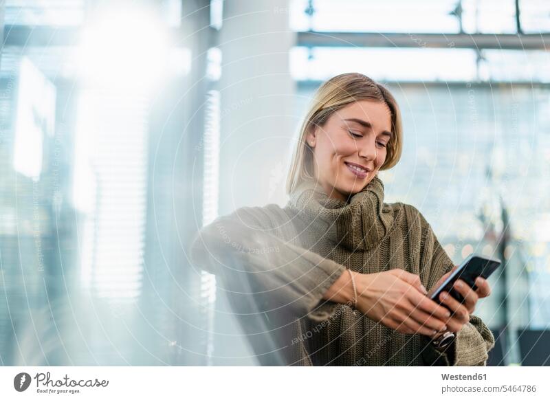 Smiling young woman sitting in waiting area using cell phone telecommunication phones telephone telephones cell phones Cellphone mobile mobile phones mobiles