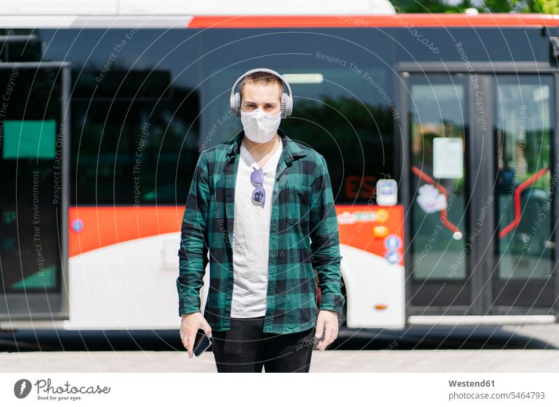 Portrait of young man wearing protective mask listening music with headphones in front of bus, Spain transport motor vehicles road vehicle road vehicles buses