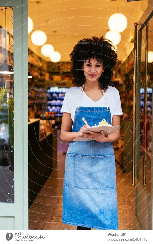 Portrait of smiling woman with clipboard standing in entrance door of a store smile clipboards clip-board clip-boards clip board shop portrait portraits