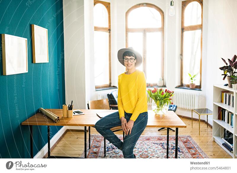 Portrait of smiling businesswoman in home office sitting on table working At Work apartment flats apartments at home Seated portrait portraits females women