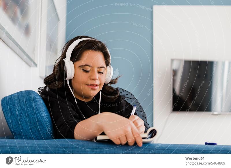 Woman with down syndrome writing in book while listening music on sofa in living room caucasian caucasian appearance caucasian ethnicity european