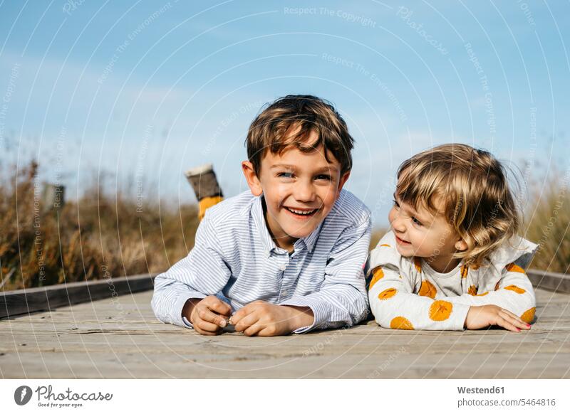 Portrait of boy and his little sister lying side by side on boardwalk having fun Harmony Harmonious paralell Juxtaposed in paralell sisters brother brothers