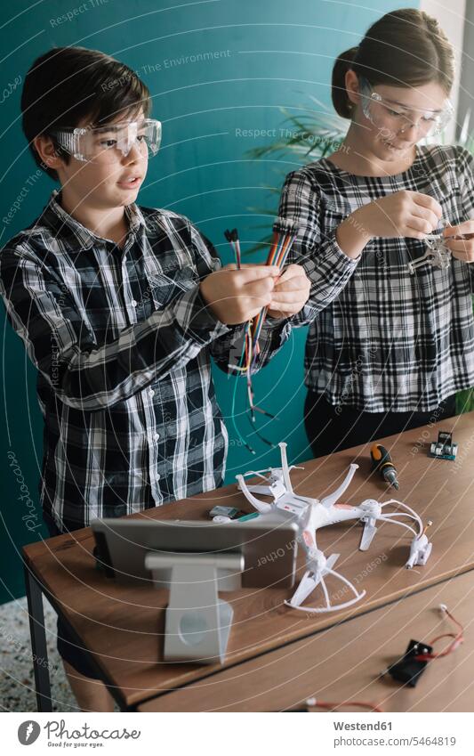 Siblings preparing drone on table while standing at home color image colour image indoors indoor shot indoor shots interior interior view Interiors