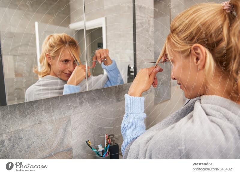 Mature woman looking in mirror cutting her own hair at home color image colour image indoors indoor shot indoor shots interior interior view Interiors day
