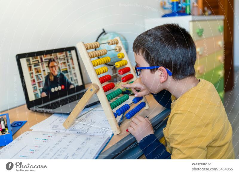 Boy with abacus at desk while teacher on video call during pandemic homeschooling color image colour image indoors indoor shot indoor shots interior
