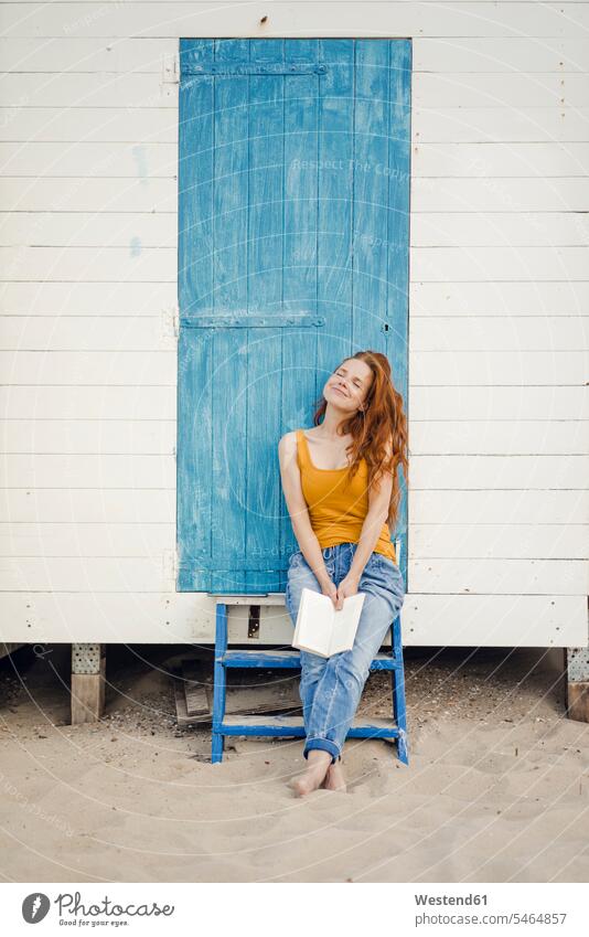 Redheaded woman sitting in front of beach cabin, reading a book beaches Beach Cabin Beach Cabins books redheaded red hair red hairs red-haired females women