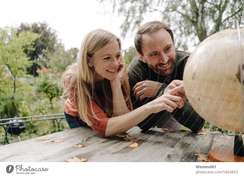 Happy couple planning to travel, looking at globe outdoors globes Tables wood wood table discover discovering smile seasons fall delight enjoyment Pleasant