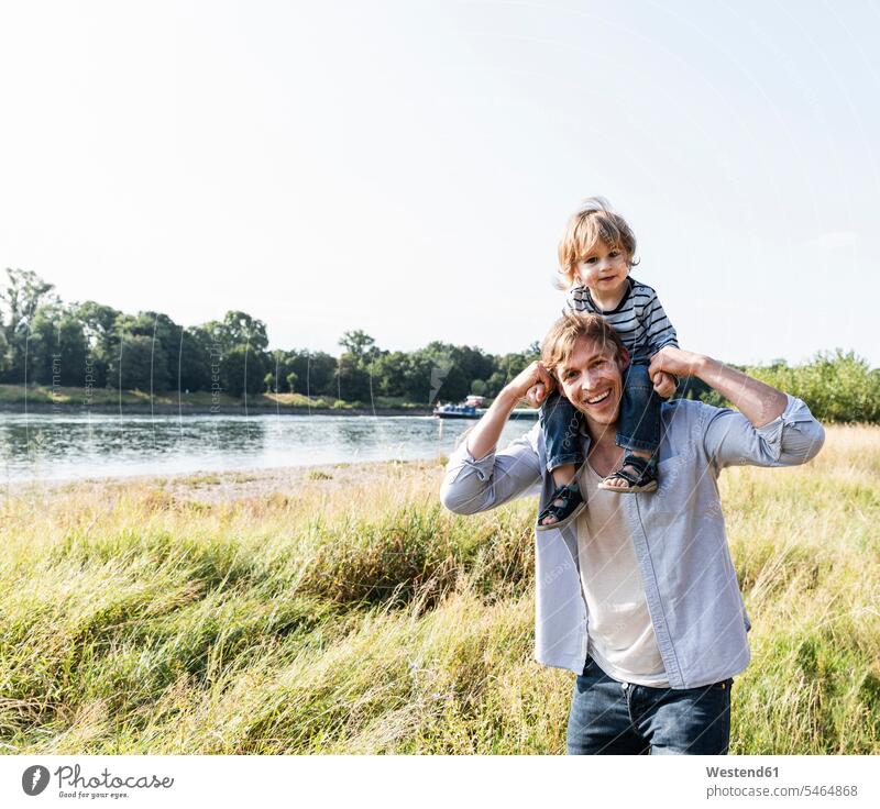 Father and son having fun at the river on a beautiful summer day Germany on shoulders childhood Stroll walk riverside riverbank togetherness confidence