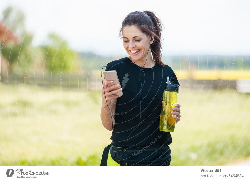 Sportive woman using smartphone during cooling break earphones ear phone ear phones water bottle water bottles bottled water cooling breaks Smartphone iPhone