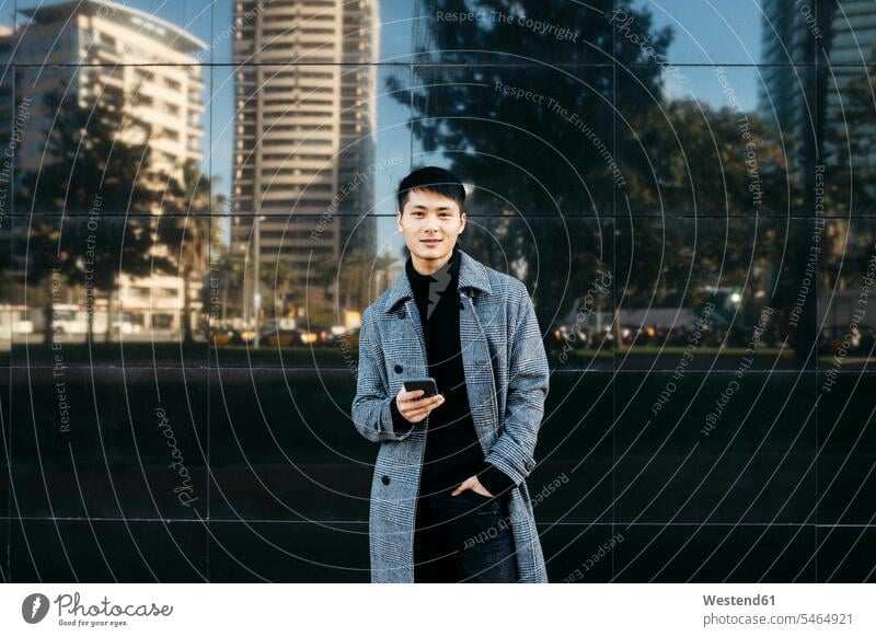 Spain, Barcelona, portrait of young man with cell phone wearing black turtleneck pullover and grey coat portraits gray Smartphone iPhone Smartphones Coat Coats
